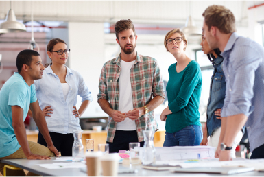 What-is-a-scrum-master-Scrum-master-vs-project manager A scrum team meets around an office table at a daily standup